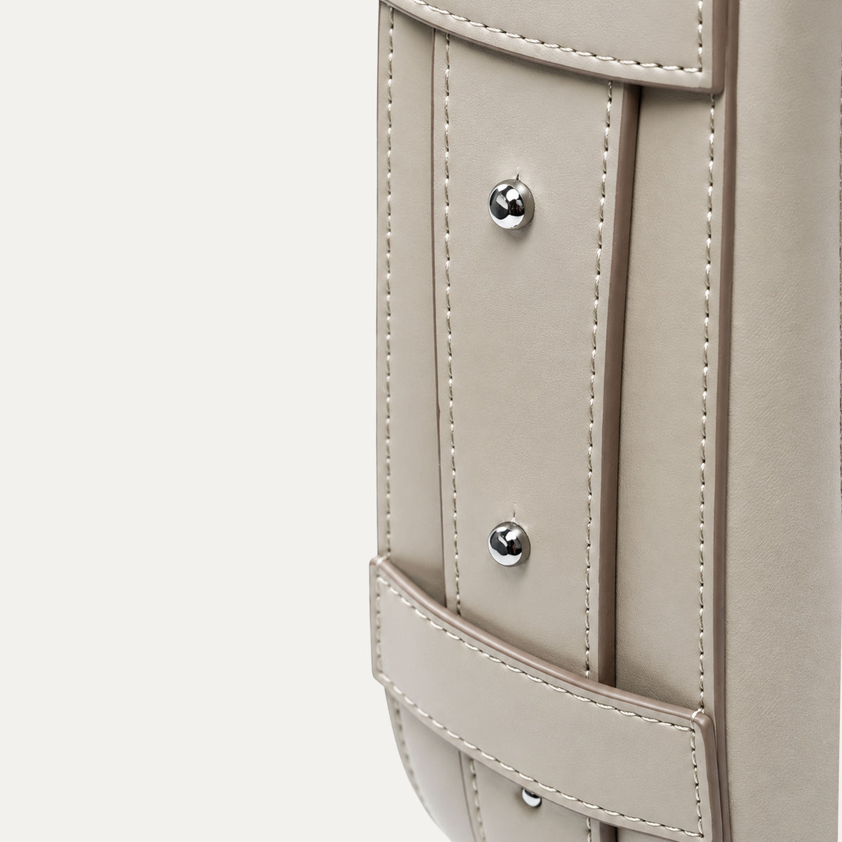Close-up detail of a taupe leather bag showing the side pocket with silver-tone rivets and stitching on a plain off-white background.