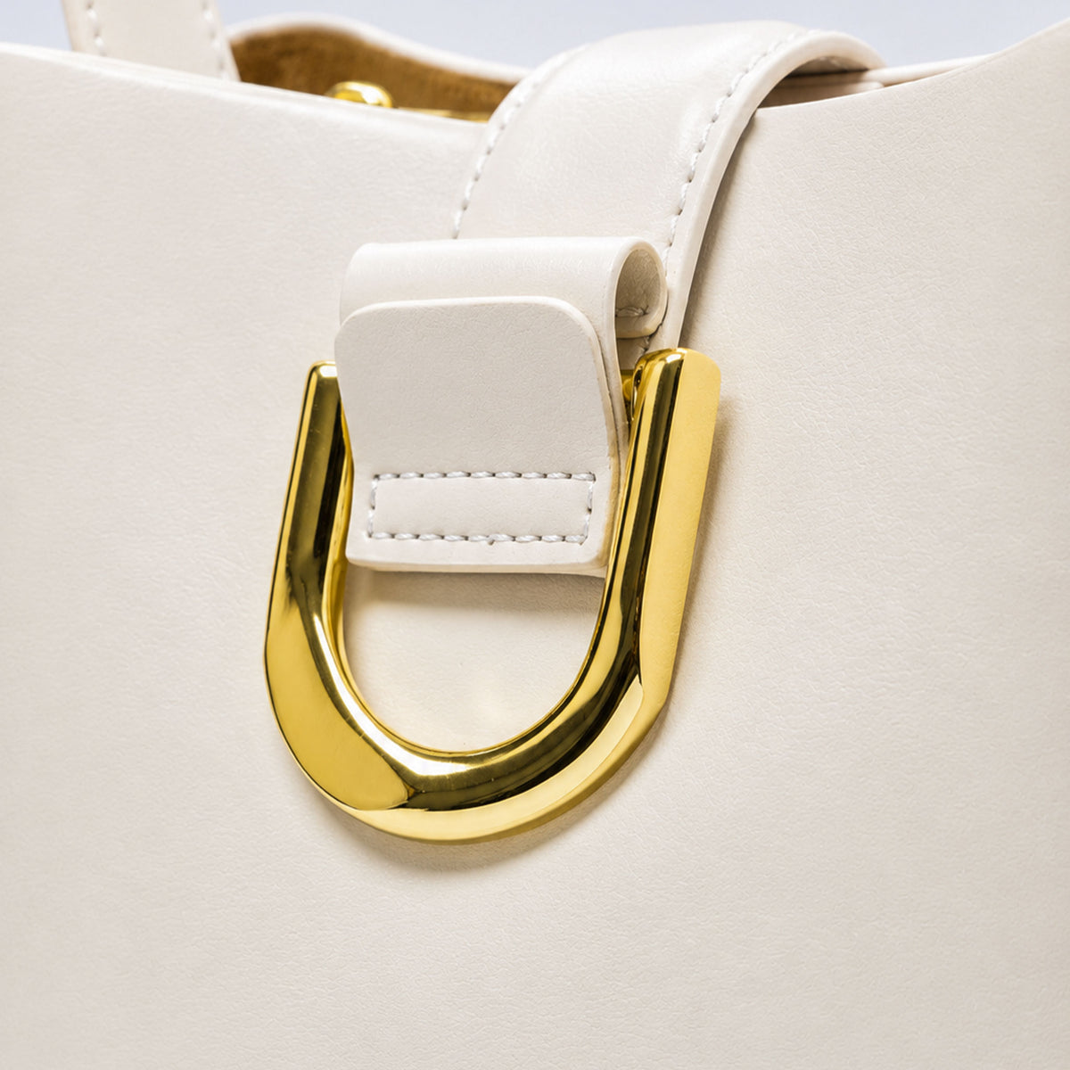 Close-up of a white leather handbag featuring a large, polished gold U-shaped metal ring clasp on the strap.