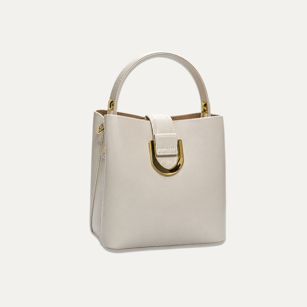 A structured cream-colored leather handbag with a top handle, a gold-tone D-ring detail on the front, and a matching shoulder strap, set against a solid off-white background.