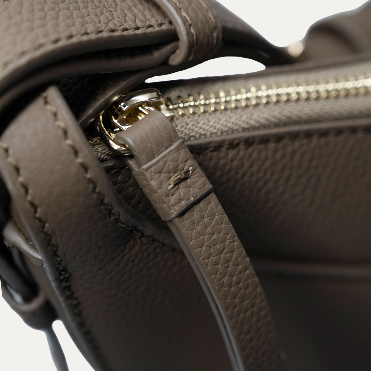 Close-up detail of a taupe leather handbag showing the pebbled texture, a matching leather strap, and gold-tone hardware.
