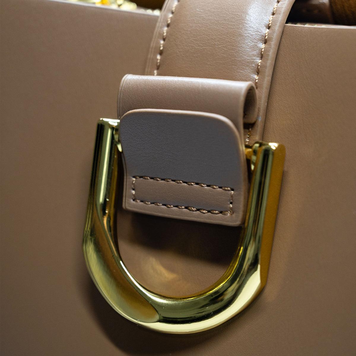 Close-up of a brown leather handbag featuring a large polished gold-tone U-shaped metal ring clasp with a matching leather keeper.
