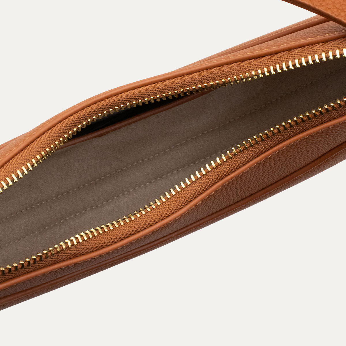 Close-up of a brown textured leather bag showing the interior lining and a gold-tone zipper against a light gray background.