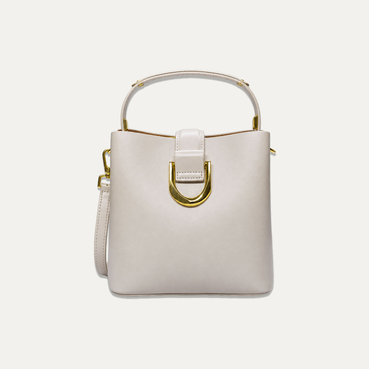 A structured bucket handbag in off-white leather with gold-tone hardware, featuring a top handle, a front strap detail, and a detachable shoulder strap, set against a solid off-white background.