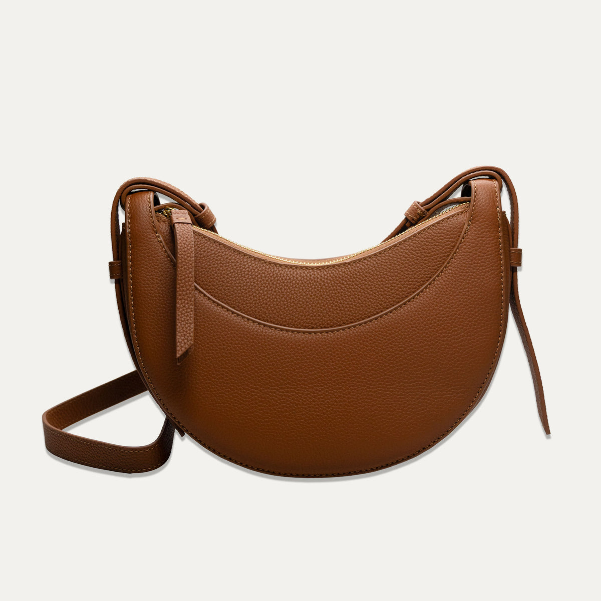 A brown pebbled leather crescent-shaped shoulder bag with a matching adjustable strap, shown against a light off-white background.