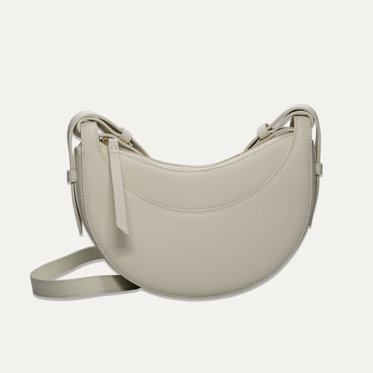 A off-white crescent-shaped leather shoulder bag with a matching adjustable strap, displayed against a solid off-white background.