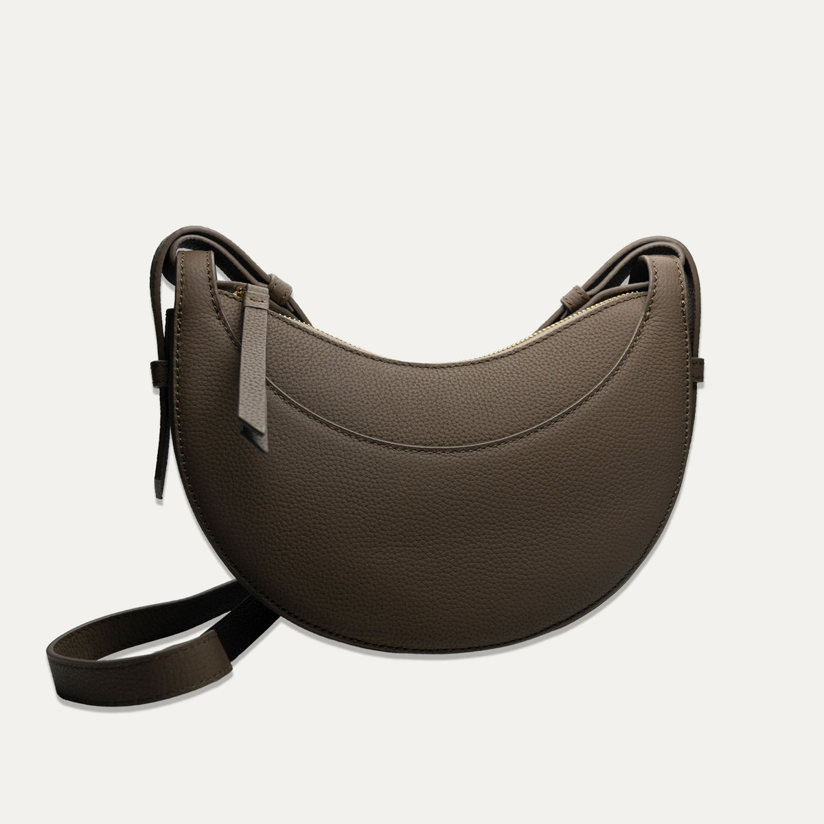 A dark brown crescent-shaped pebbled leather shoulder bag with a matching adjustable strap, displayed on a light off-white background.