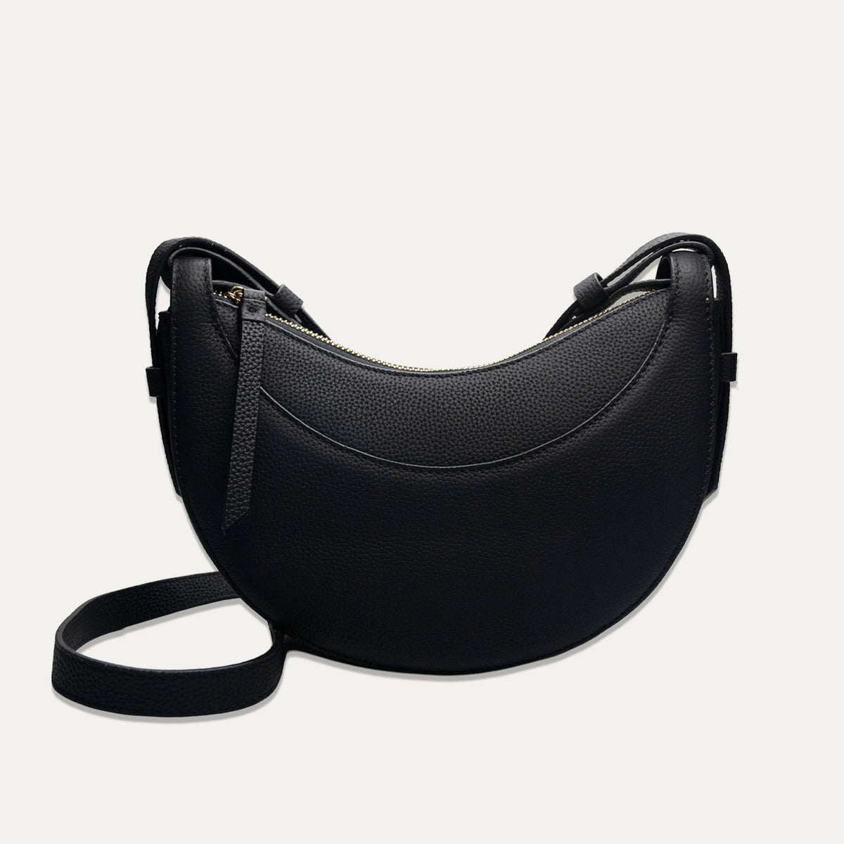 A black crescent-shaped pebbled leather shoulder bag with a matching black strap, shown against a light off-white background.