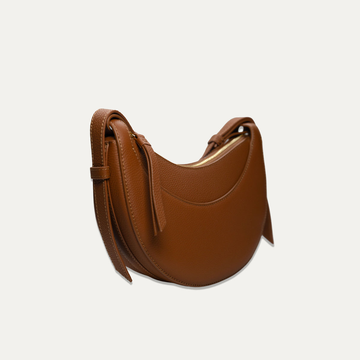 A brown pebbled leather crescent-shaped shoulder bag with a matching strap, shown on a light off-white background.