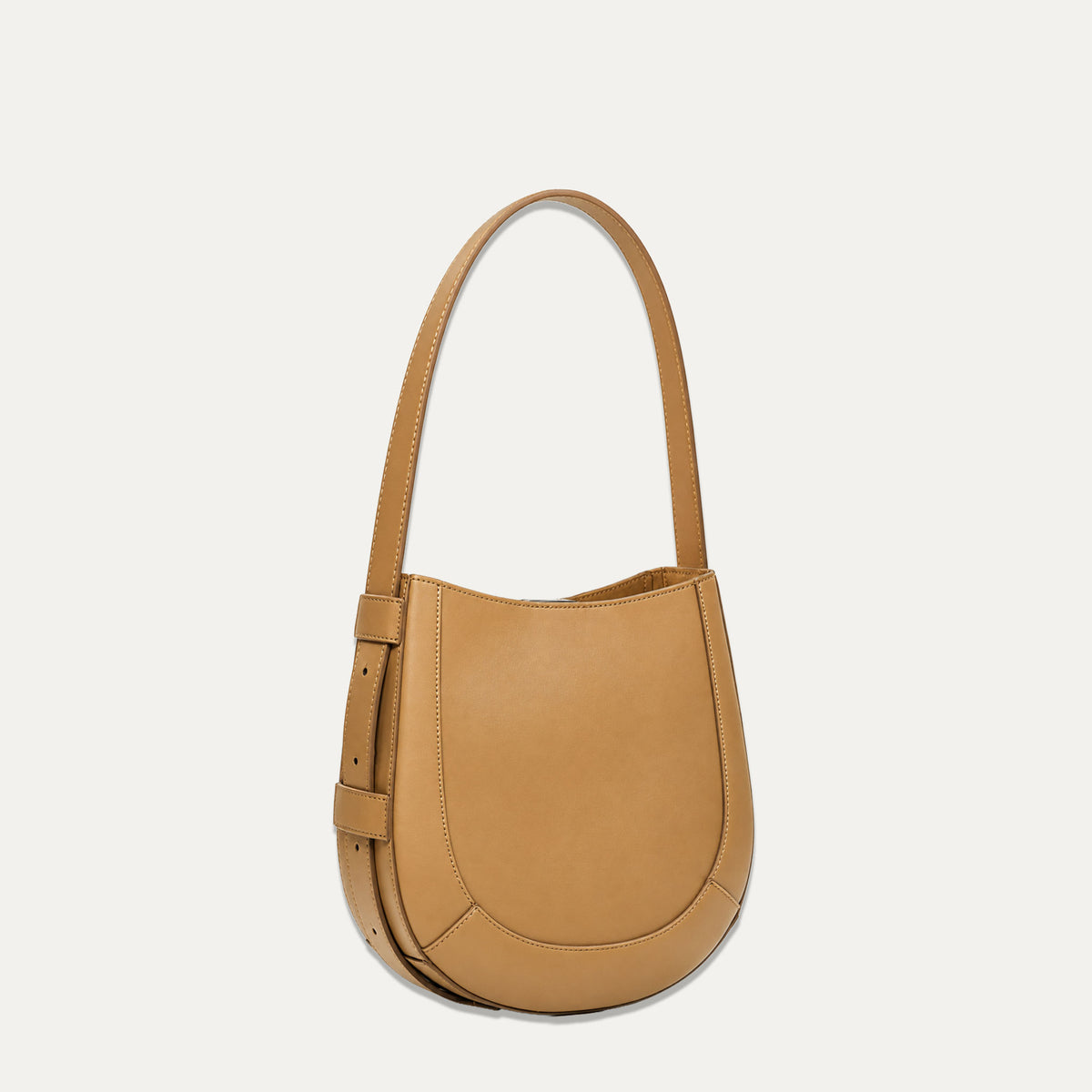A tan leather crescent-shaped shoulder bag with a single top handle and a side buckle detail, shown against a plain off-white background.