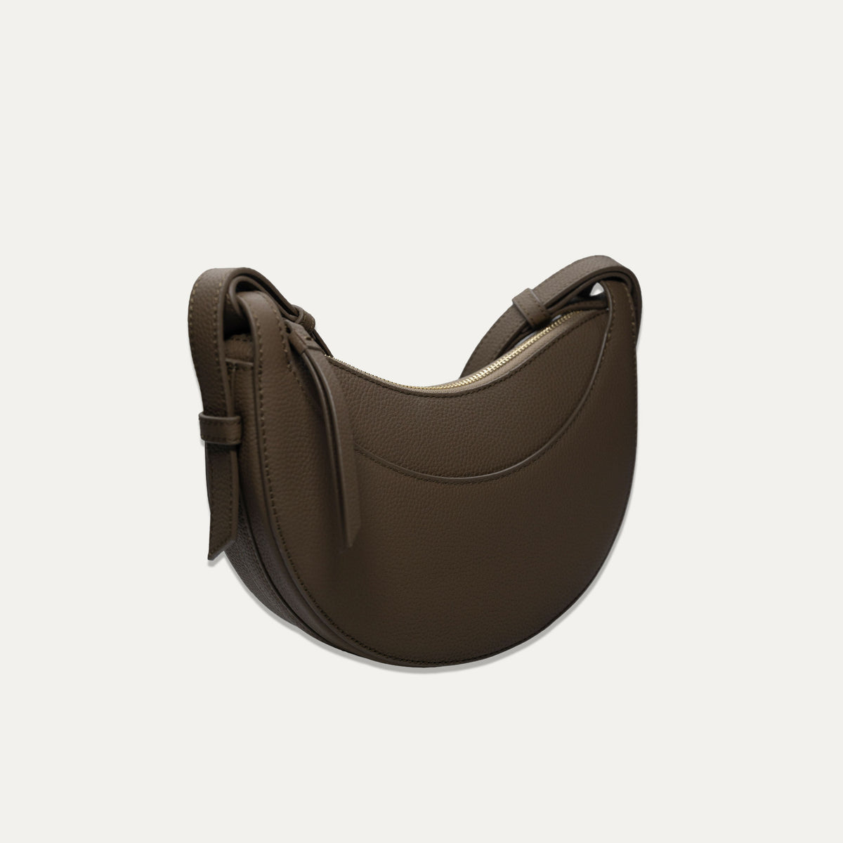 A dark brown crescent-shaped leather shoulder bag with a matching adjustable strap, shown on a light off-white background.